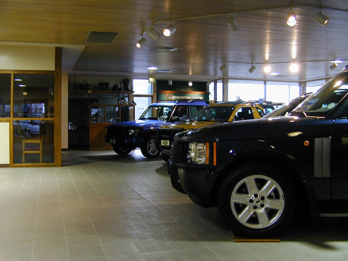Vehicles on the polished tile floor of a car dealership showroom, the service area visible through glass behind