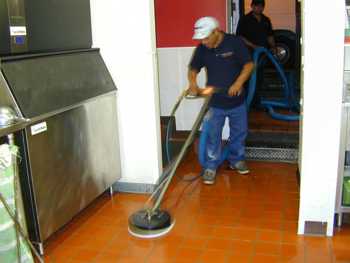 An operator working a floor machine across orange quarry tile in a service corridor