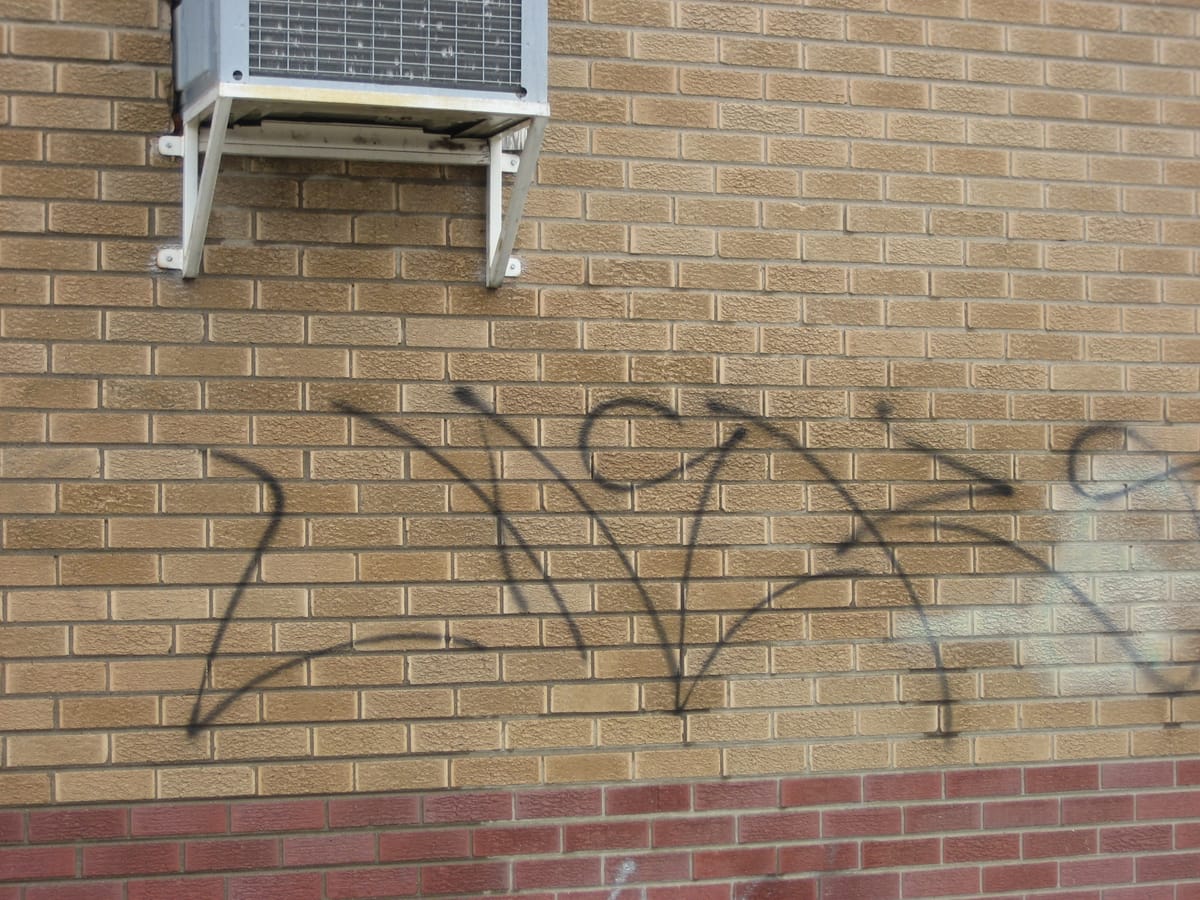 Black spray-paint tagging across the brickwork of a commercial building