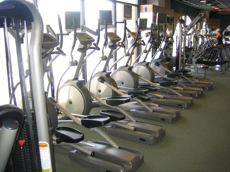 A long rank of elliptical trainers and screens on the cardio floor of a health club