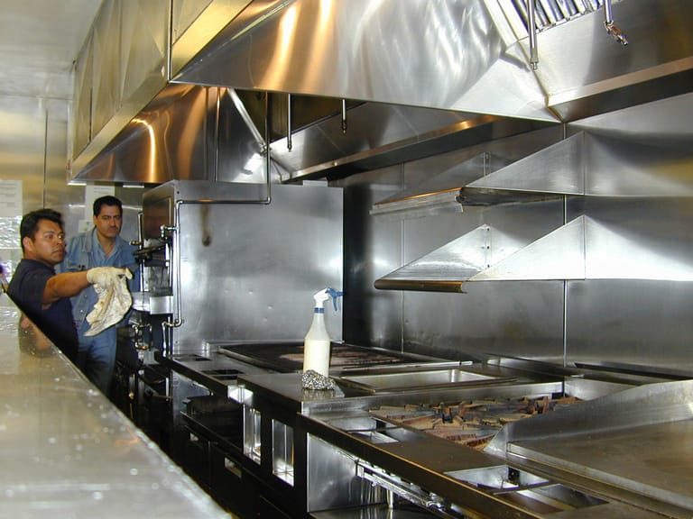 Two workers cleaning the stainless steel line and extraction hood of a commercial kitchen