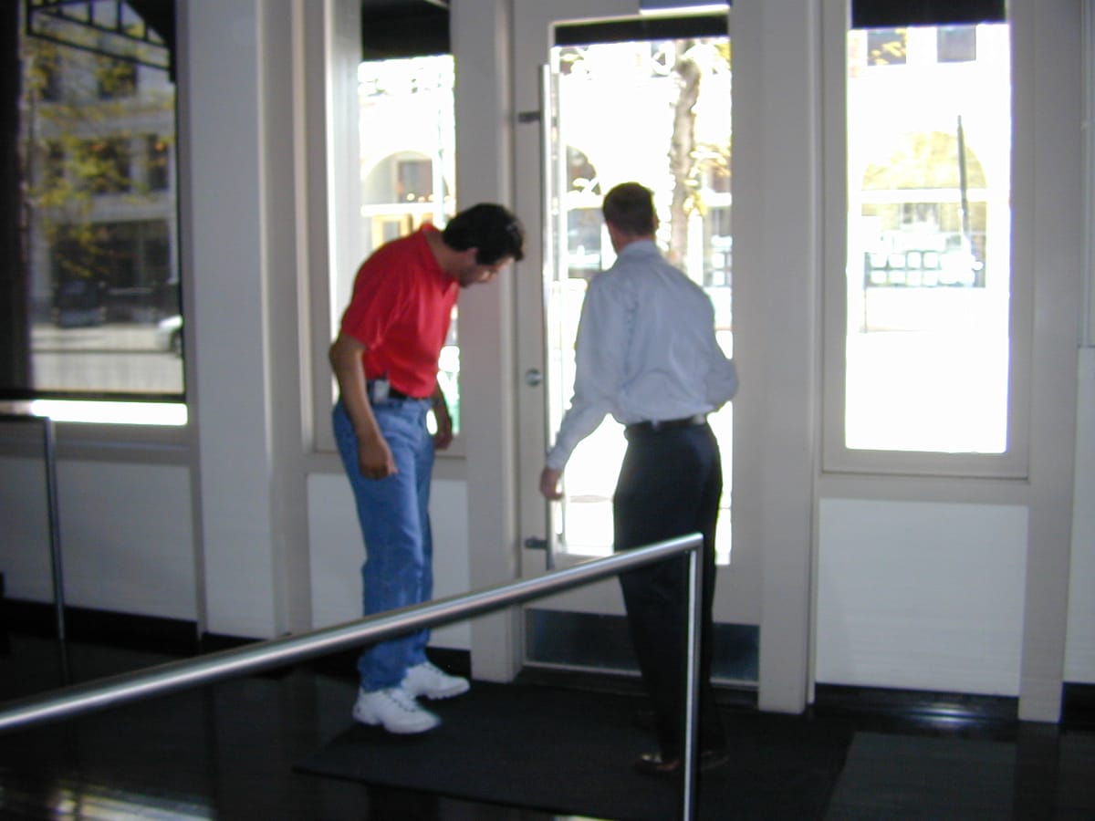 Two people at the glass entrance doors of an office lobby, daylight across the floor