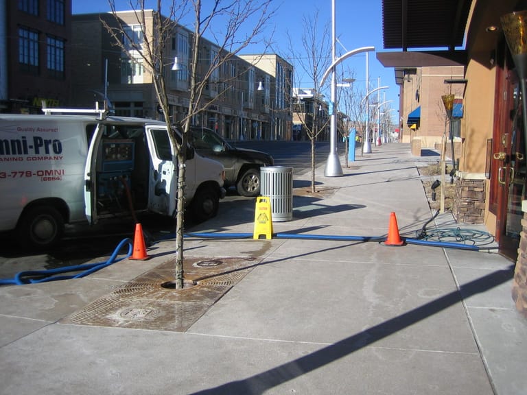 The OmniPro Cleaning Company van parked on a Denver street with cones set out and a hose run into a storefront