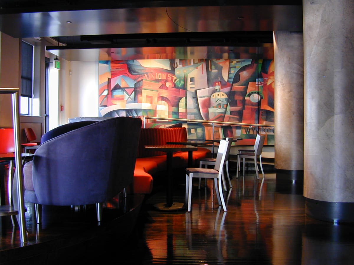 A restaurant dining room after service, banquettes and chairs beside a painted mural, the wood floor polished to a reflection
