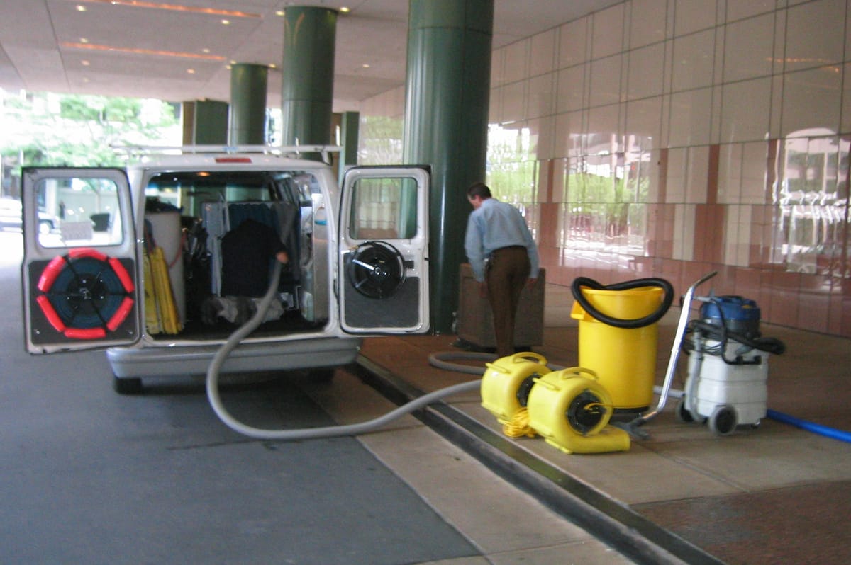 A van-mounted extraction unit backed up to an office lobby with hoses run inside and yellow air movers staged on the walkway